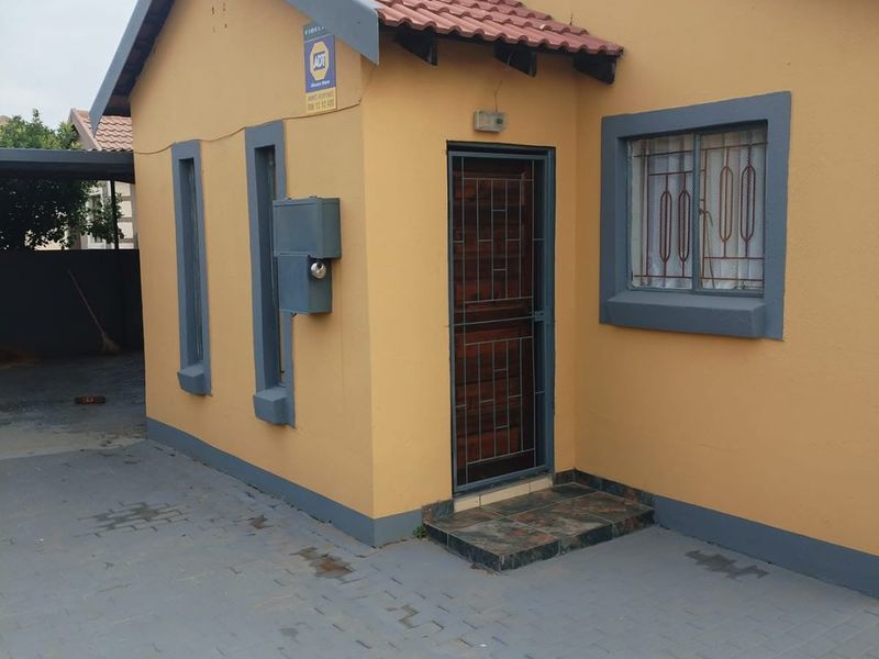 Front exterior view of a single-story house featuring a paved driveway, tiled roof, and secure entrance with security gate and window bars.