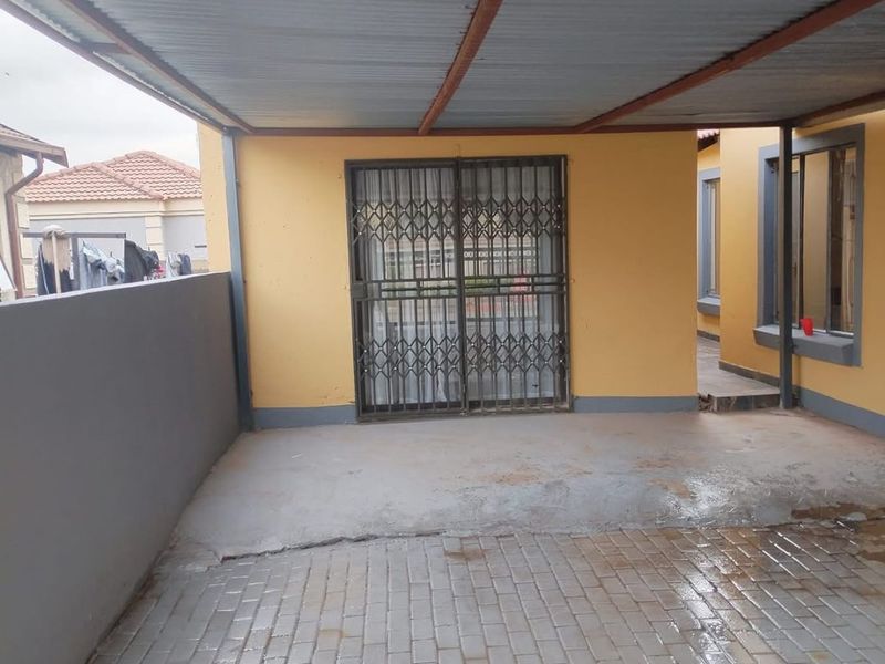 A covered outdoor patio area featuring paved flooring, a corrugated metal roof structure, and a security gate entrance.