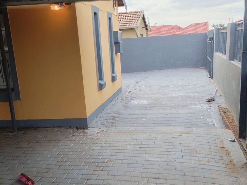 A covered carport area featuring a paved driveway, corrugated metal roofing, and a secure boundary wall.