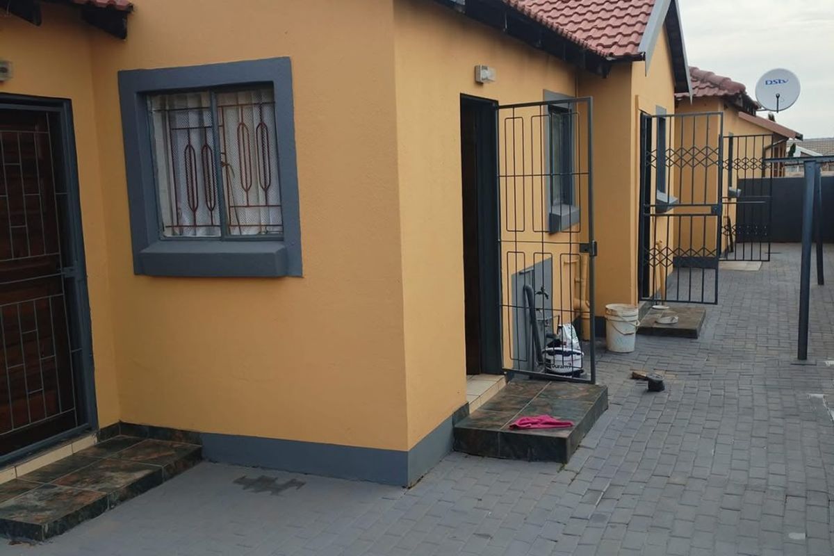 Exterior view of a residential property featuring a paved courtyard, tiled roof, and security gates on the entrances.