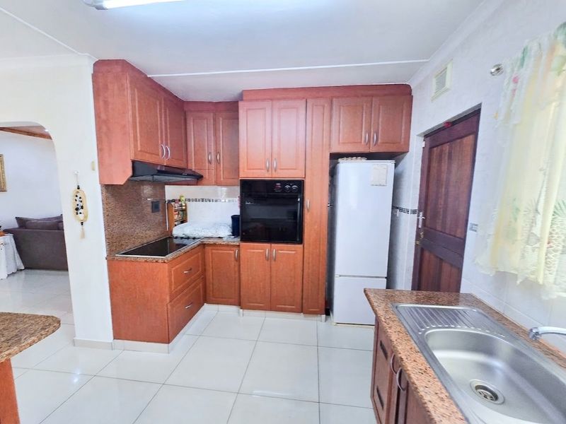 Functional kitchen featuring granite countertops, wooden cabinetry, built-in oven, electric hob, and tiled flooring, offering a practical layout for daily meal preparation.