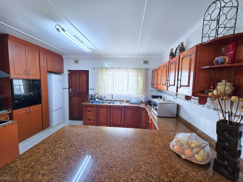 A functional kitchen featuring warm-toned wooden cabinetry, granite countertops, and a double bowl sink, offering a classic layout with ample storage space.
