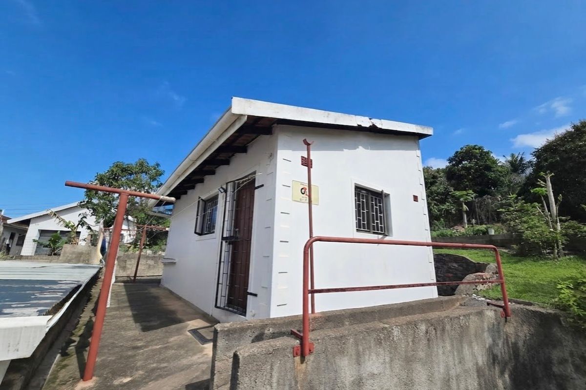 Rear view of a small outbuilding featuring a concrete retaining wall, metal security bars on windows, and a metal safety railing.