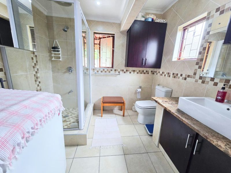 A functional bathroom featuring a glass-enclosed shower, a modern vessel sink on a granite vanity, and neutral wall and floor tiling.
