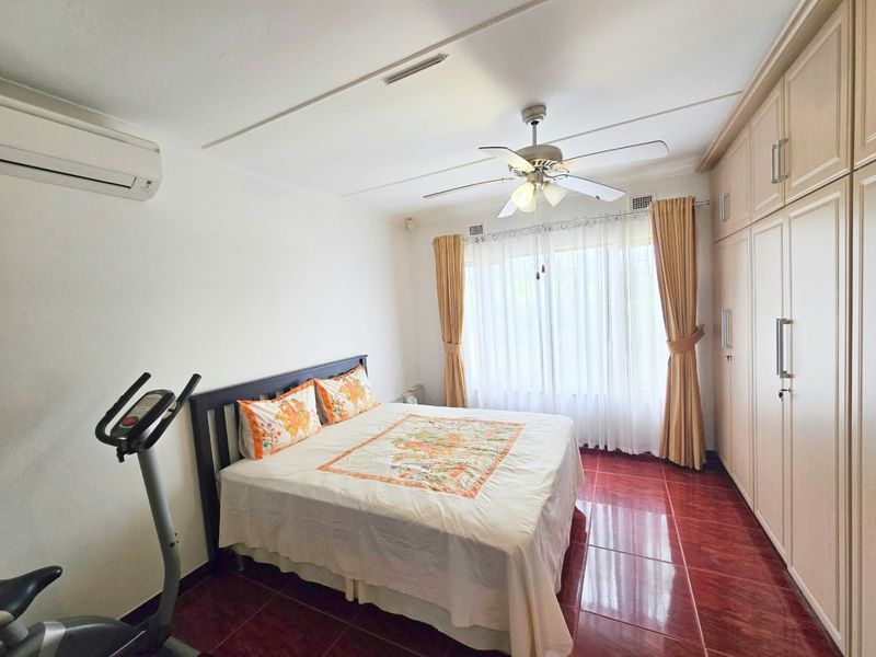 A bedroom featuring built-in cupboards, a ceiling fan, and a split-system air conditioner, finished with tiled flooring.