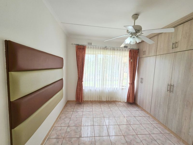 A bright, empty bedroom featuring tiled flooring, built-in wooden cupboards, and a ceiling fan, offering a clean canvas for personalization.