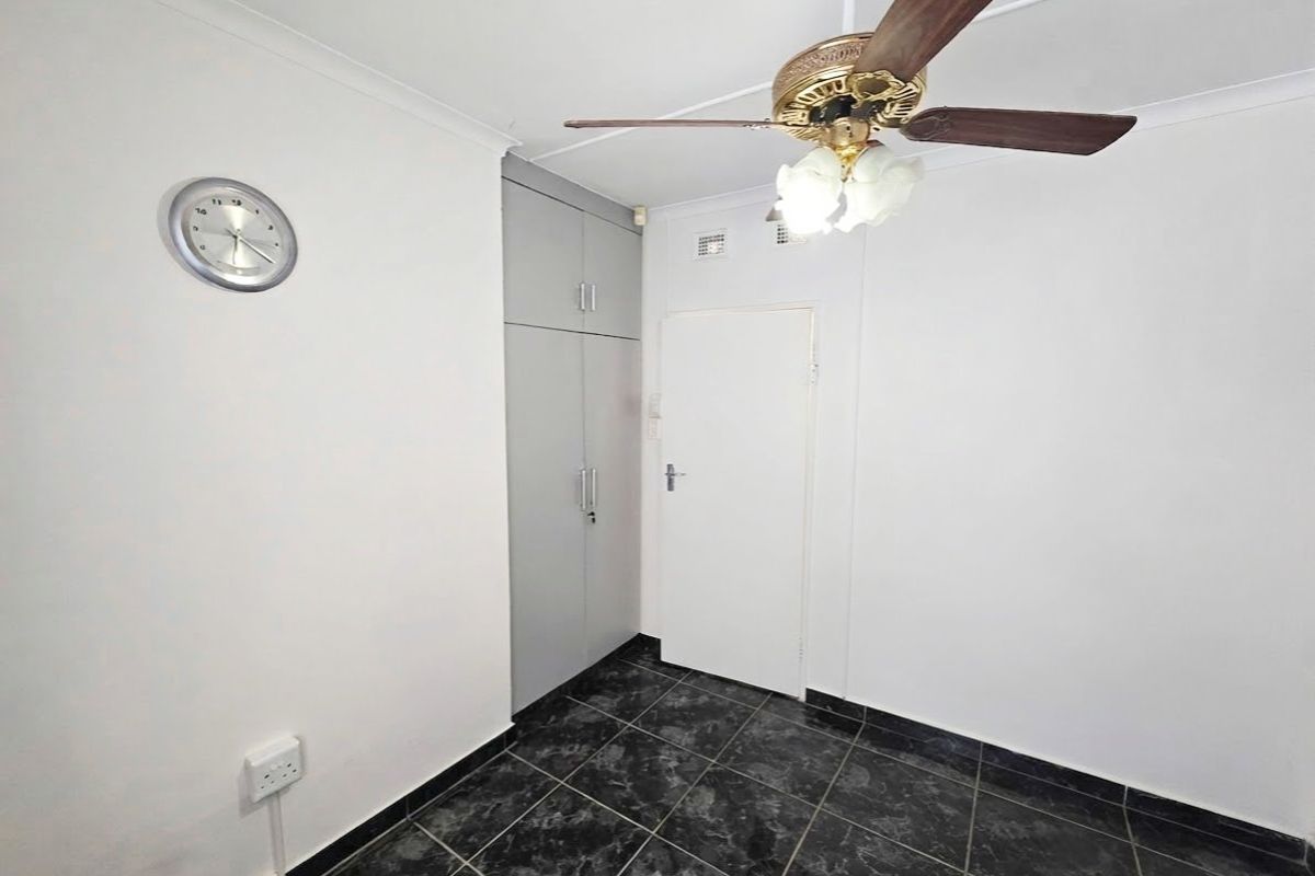 A clean, empty bedroom featuring dark tiled flooring, built-in storage cupboards, and a ceiling fan.