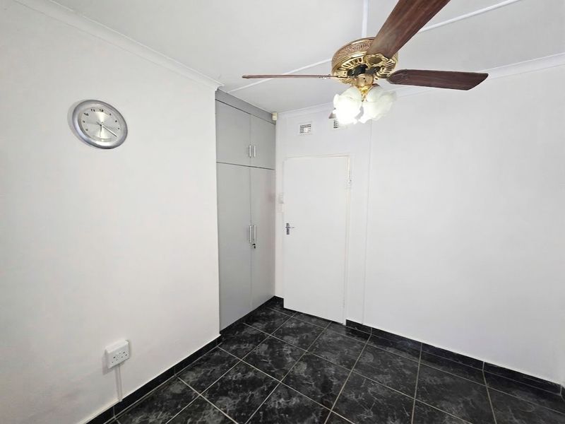 A clean, empty bedroom featuring dark tiled flooring, built-in storage cupboards, and a ceiling fan.