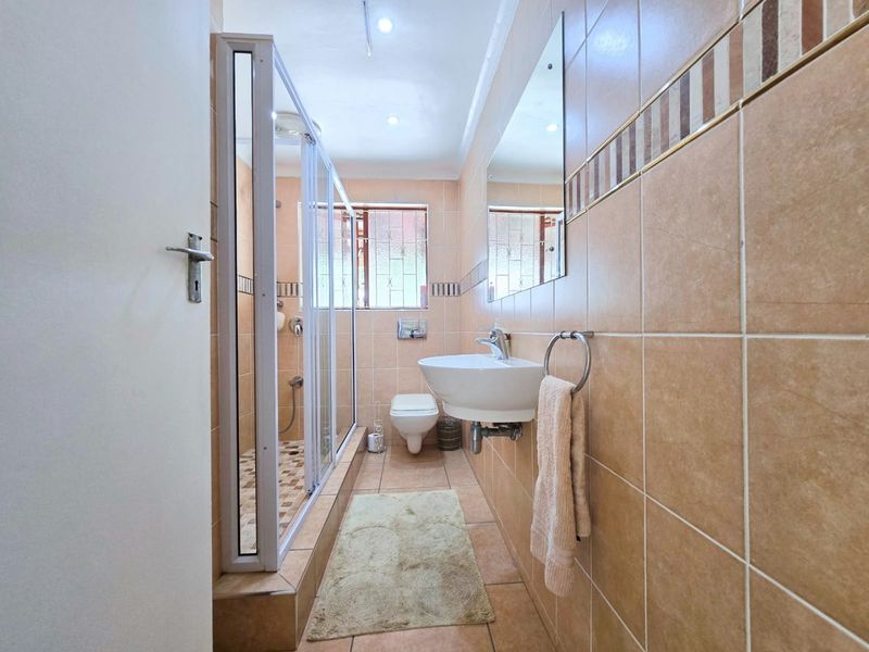 A functional bathroom featuring a shower enclosure, wall-mounted basin, and wall-hung toilet, finished with neutral wall and floor tiling.