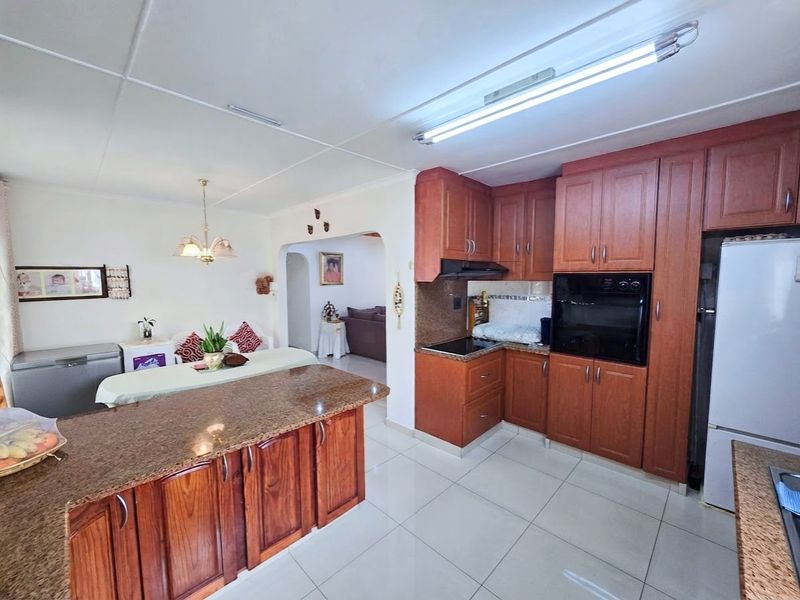 Open-plan kitchen and dining area featuring granite countertops, warm-toned wooden cabinetry, built-in oven, and tiled flooring throughout.