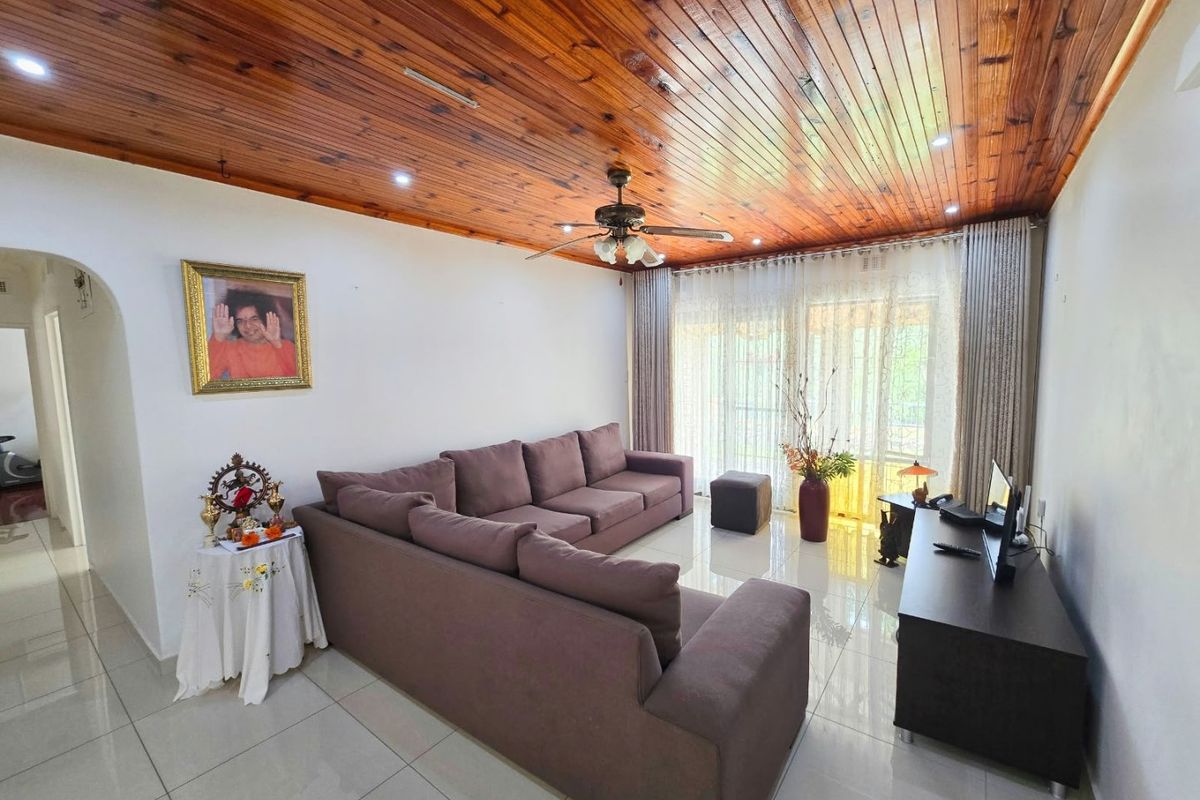 A well-maintained living room featuring polished tiled floors, a warm timber tongue and groove ceiling, and large sliding doors providing natural light.