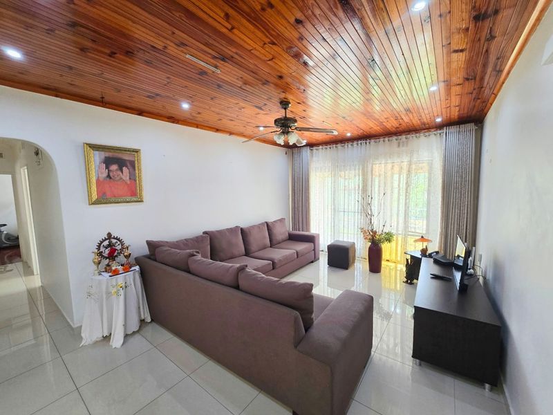 A well-maintained living room featuring polished tiled floors, a warm timber tongue and groove ceiling, and large sliding doors providing natural light.
