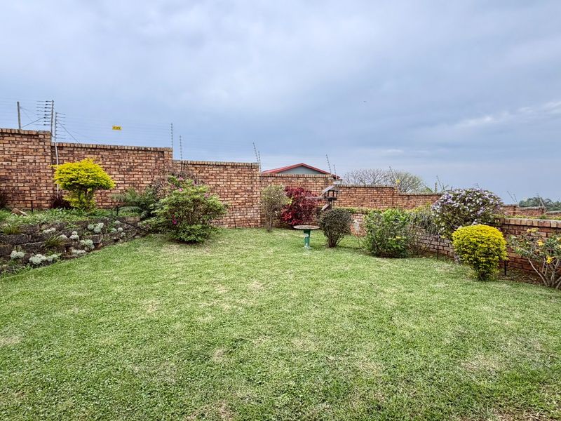 A well-maintained private garden featuring a lush lawn, established shrubs, and secure brick boundary walls with integrated electric fencing.