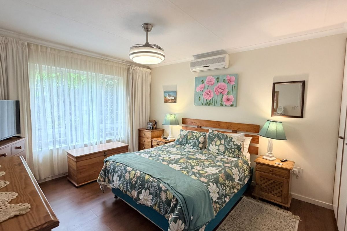 A well-maintained bedroom featuring laminate flooring, a ceiling fan, a split-system air conditioner, and built-in storage cupboards.