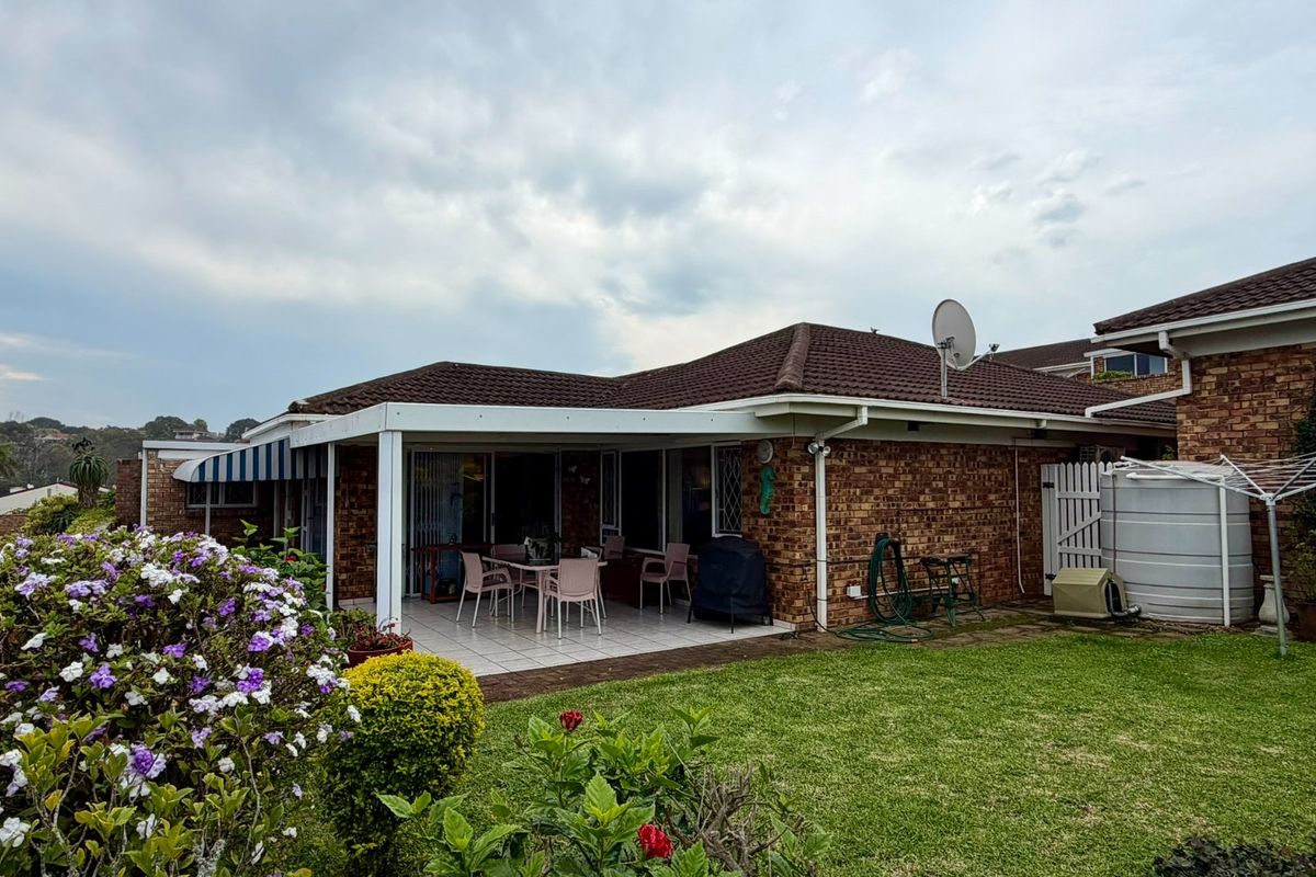 Rear view of the townhouse featuring a covered tiled patio, brick exterior, and a private garden area with a water storage tank.