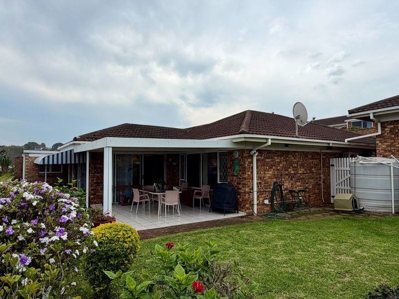 Rear view of the townhouse featuring a covered tiled patio, brick exterior, and a private garden area with a water storage tank.