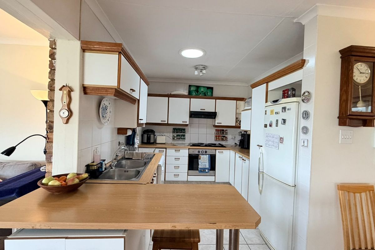 A functional kitchen featuring white cabinetry with wood trim, a breakfast bar, built-in oven, gas hob, and tiled splashbacks.