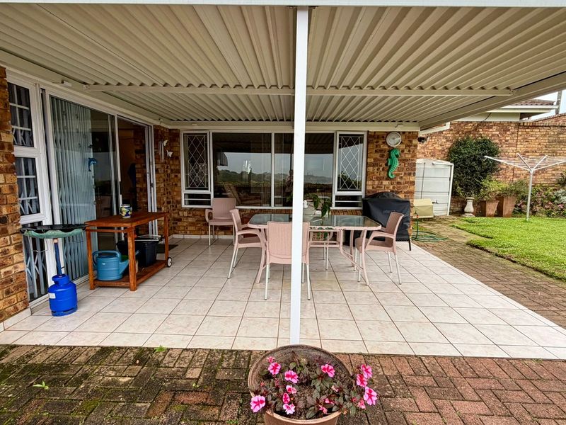 Covered outdoor patio featuring tiled flooring and direct access to the living area through sliding glass doors, overlooking a private garden space.