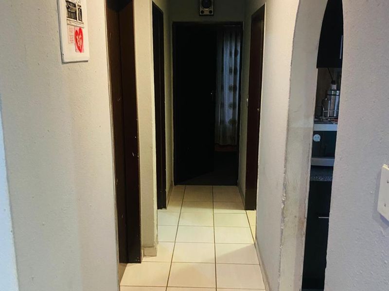A functional hallway featuring tiled flooring and an arched entryway leading to adjacent rooms, showing signs of wear on the wall finishes.