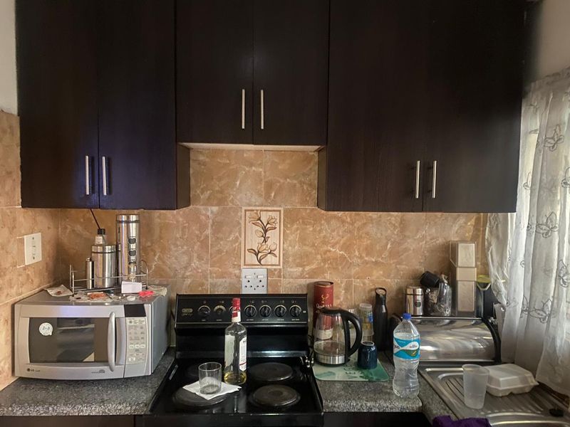 A functional kitchen featuring dark wood cabinetry, stone-look tile backsplash, granite countertops, and a built-in electric stove.