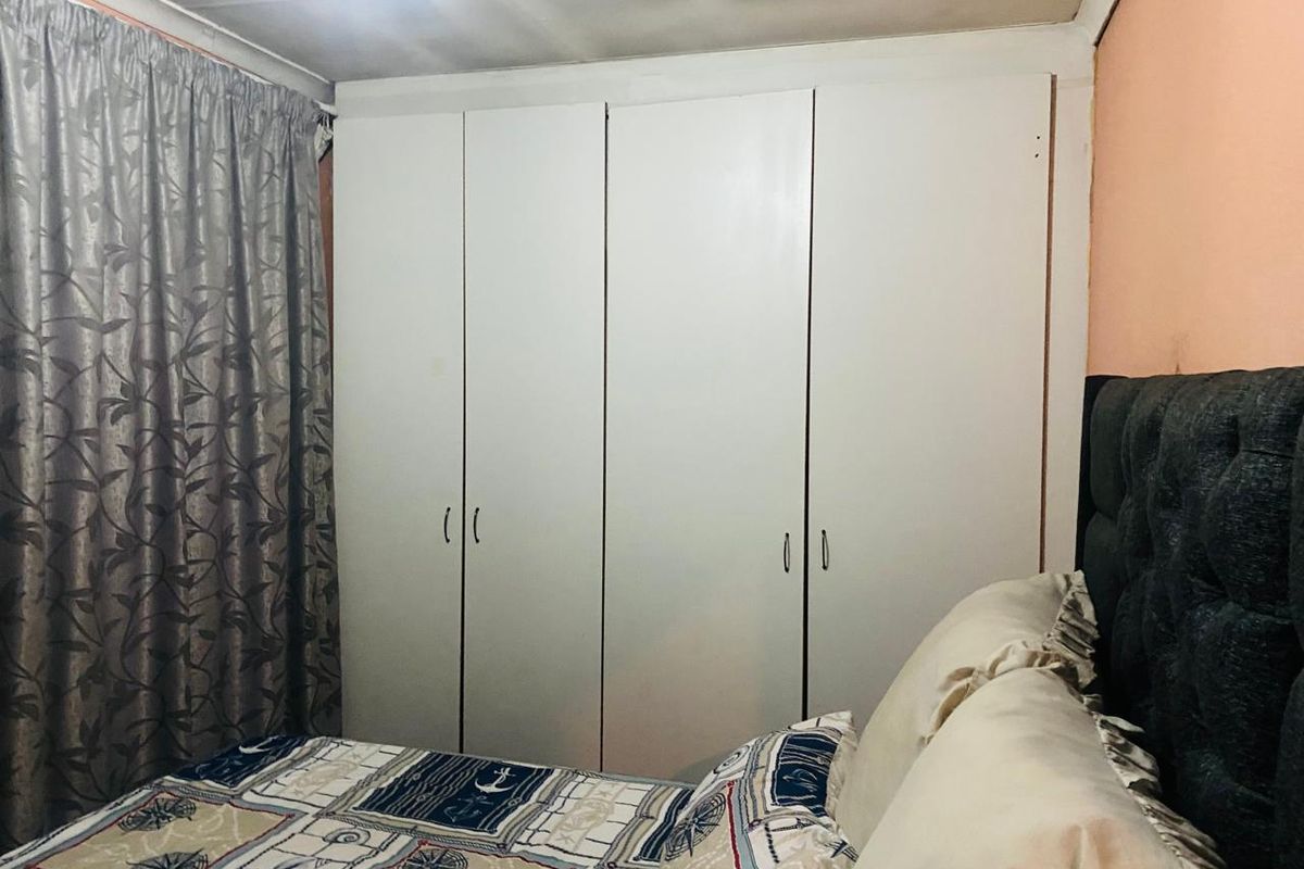 A bedroom featuring a large white built-in wardrobe and coved ceiling, requiring cosmetic updates to the wall and ceiling finishes.