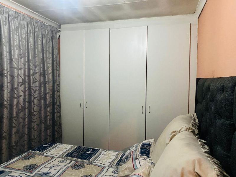 A bedroom featuring a large white built-in wardrobe and coved ceiling, requiring cosmetic updates to the wall and ceiling finishes.