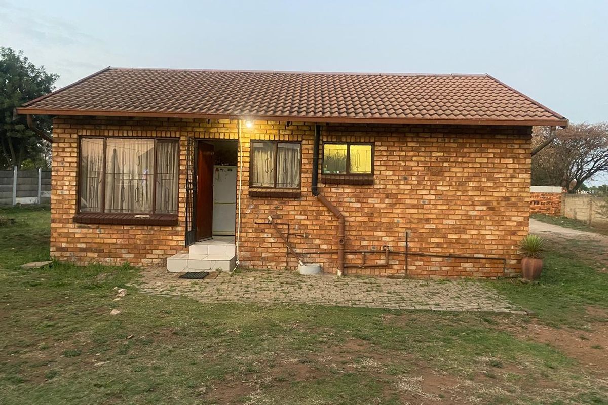 A single-story face brick house featuring a tiled roof, paved patio area, and aluminium window frames, set within a modest garden.