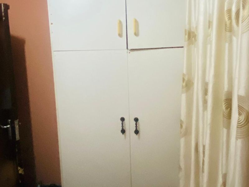A bedroom featuring a white built-in wardrobe with mismatched handles and misaligned doors.