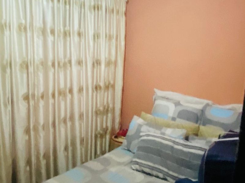 A compact bedroom featuring peach-toned walls and floor-to-ceiling curtains, offering a simple and functional sleeping space.