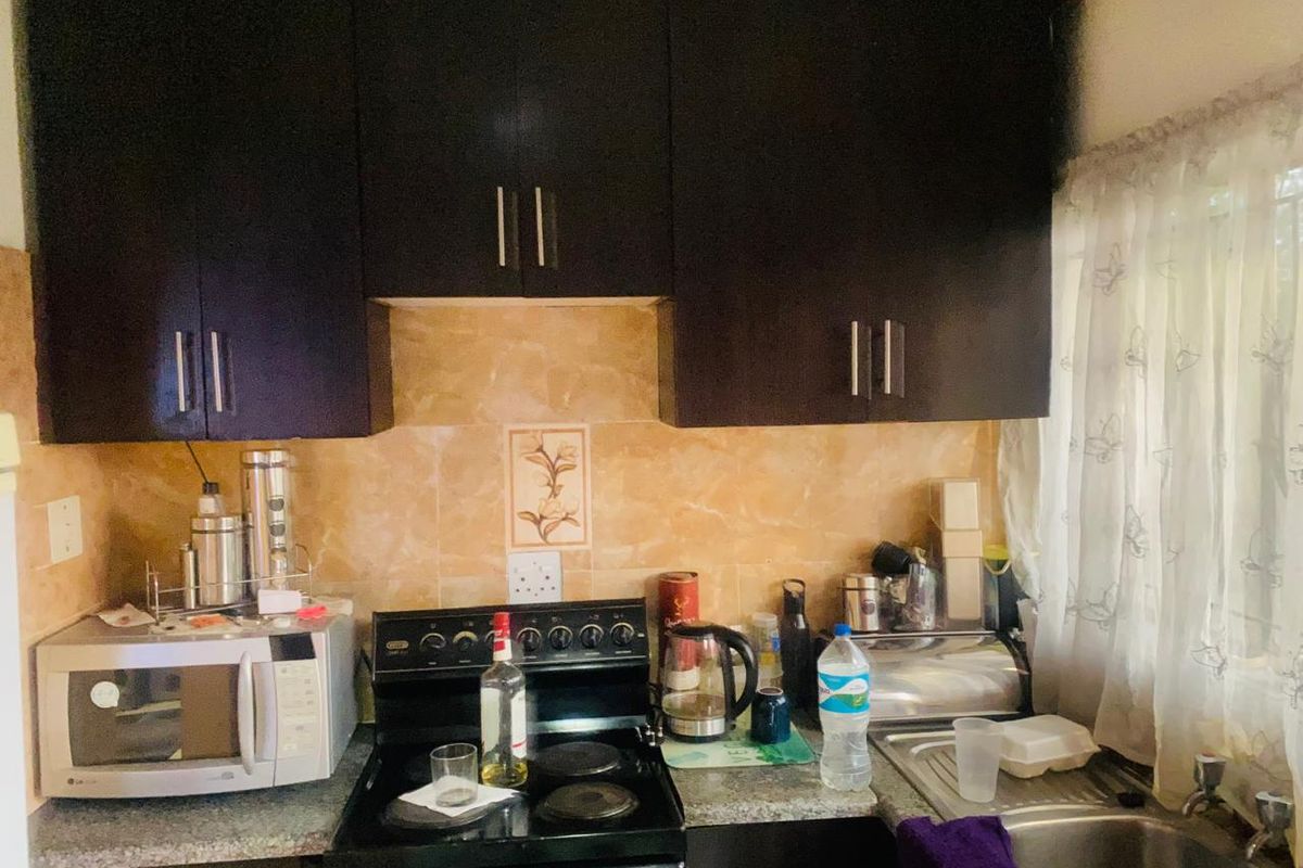 Compact kitchen featuring dark wood cabinetry, a stone-look tiled backsplash, laminate countertops, and a functional freestanding electric stove.