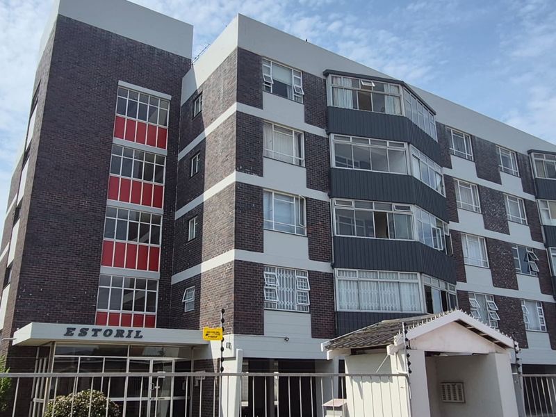 Exterior view of the Estoril apartment building, featuring a multi-story brick facade with aluminum windows and secure perimeter fencing.