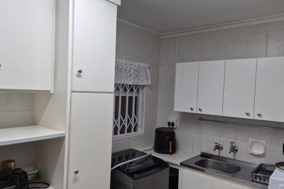 A functional kitchen area featuring white built-in cabinetry, a stainless steel sink, and tiled wall finishes with a window security gate.