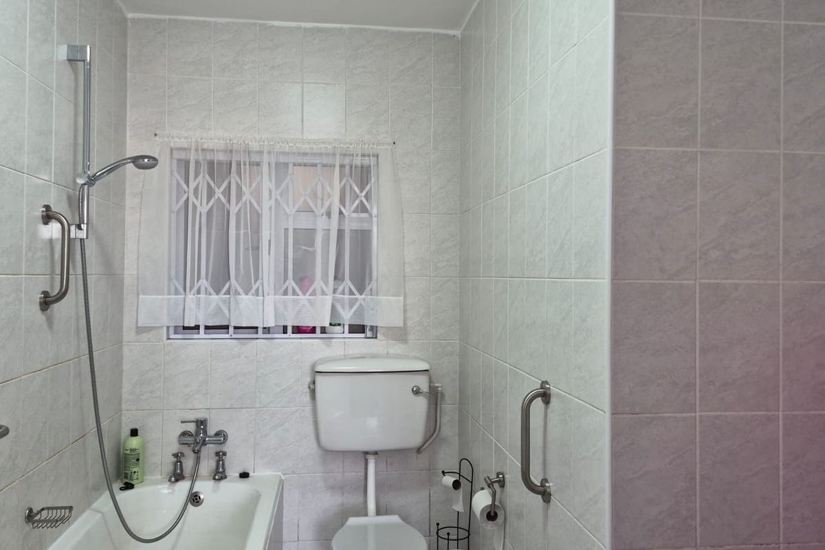 A functional bathroom featuring a bathtub with a handheld shower, toilet, and safety grab rails, finished with neutral ceramic wall tiles.