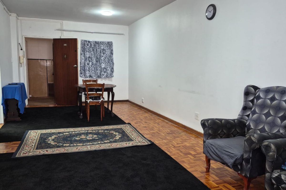 Spacious living area featuring original parquet flooring and a built-in cupboard, offering a versatile layout for comfortable apartment living.