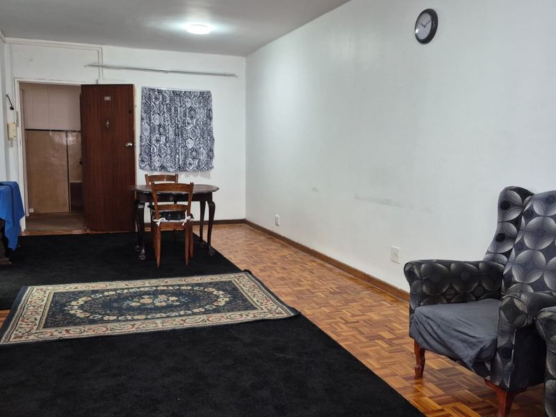 Spacious living area featuring original parquet flooring and a built-in cupboard, offering a versatile layout for comfortable apartment living.