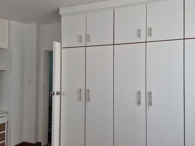 A clean bedroom featuring extensive white built-in cupboards with ample storage and a matching built-in vanity area with an integrated mirror.
