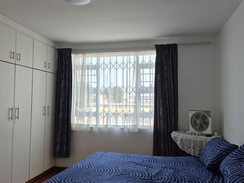 A bedroom featuring white built-in cupboards and a window fitted with a security gate.