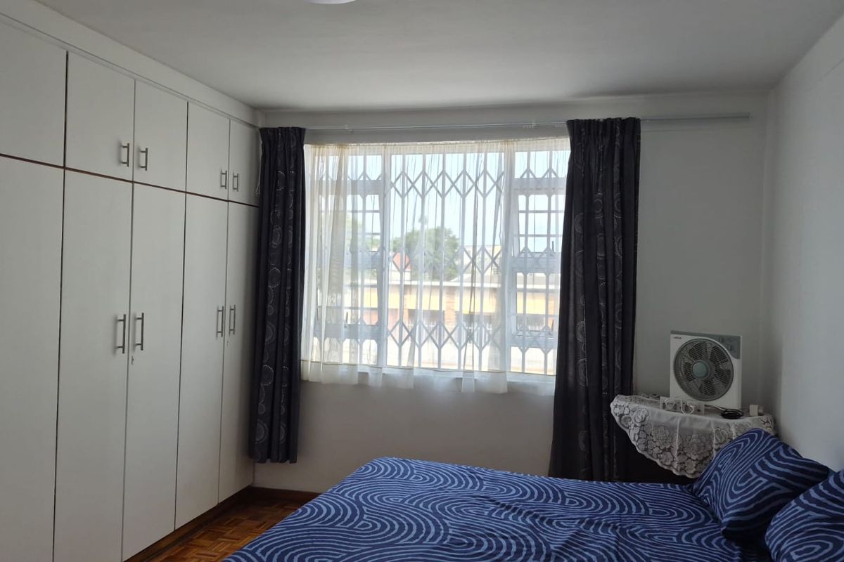 A bedroom featuring extensive built-in cupboards, parquet flooring, and a window fitted with a security gate.
