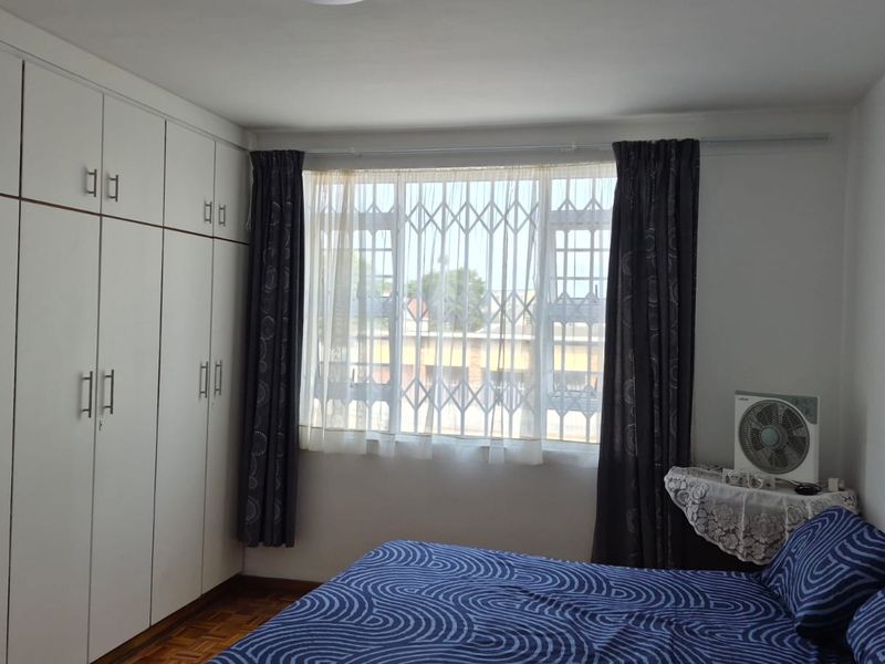 A bedroom featuring extensive built-in cupboards, parquet flooring, and a window fitted with a security gate.