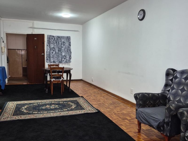 A living area featuring original parquet flooring and a built-in cupboard, offering a functional space with potential for cosmetic updates.