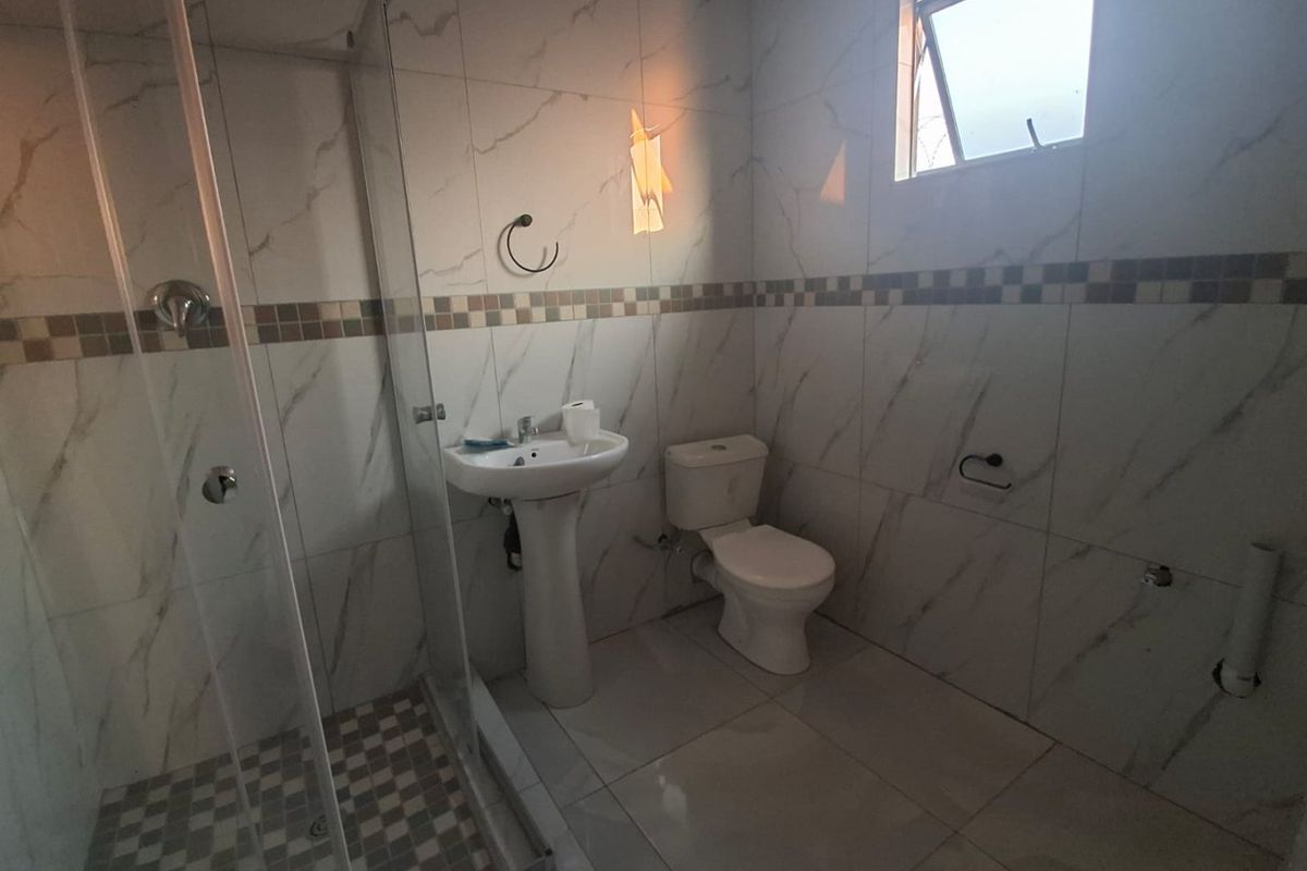 A clean, modern bathroom featuring a glass-enclosed shower, pedestal basin, and toilet with neutral marble-look wall tiles and matching floor tiles.