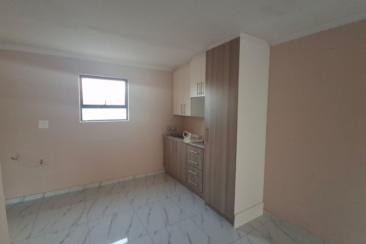 A compact, empty kitchen area featuring modern tiled flooring, built-in cabinetry, and a sink, offering a clean and functional space ready for customization.