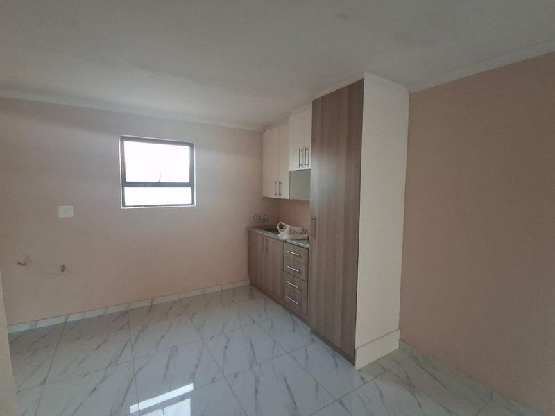 A compact, empty kitchen area featuring modern tiled flooring, built-in cabinetry, and a sink, offering a clean and functional space ready for customization.
