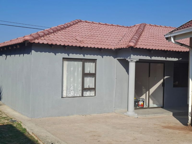 Rear view of the property featuring a tiled roof, grey exterior walls, a sliding glass door, and a paved patio area.