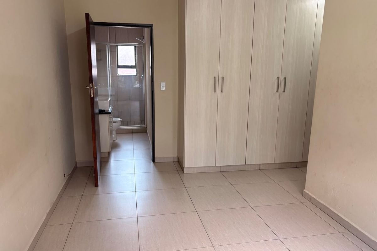 A clean, empty bedroom featuring neutral tiled flooring and ample built-in cupboard storage, with direct access to an en-suite bathroom.