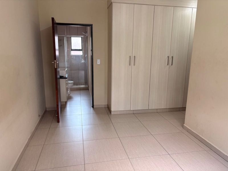 A clean, empty bedroom featuring neutral tiled flooring and ample built-in cupboard storage, with direct access to an en-suite bathroom.