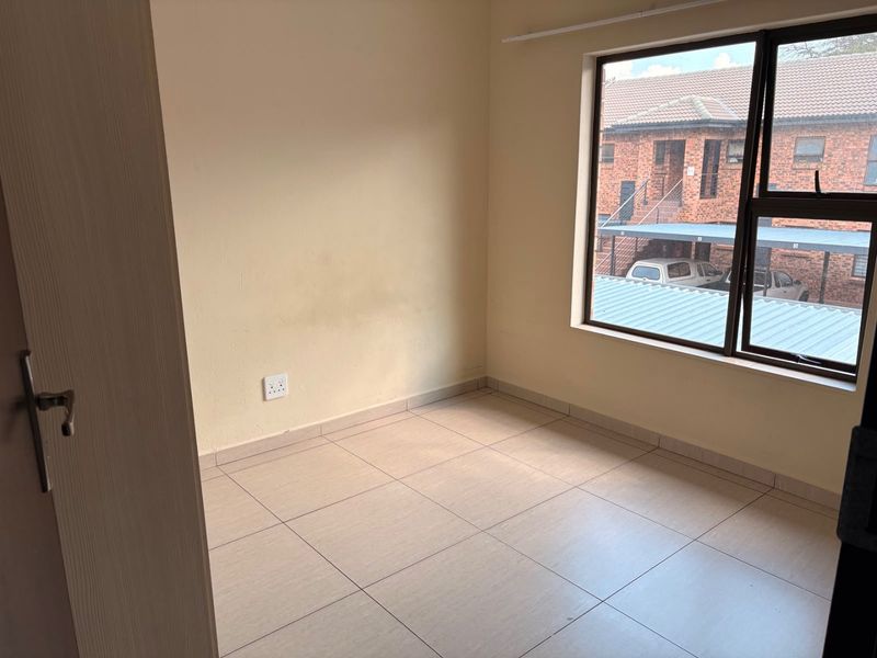 An empty bedroom featuring tiled flooring and a large aluminium window, providing a blank canvas for personalization.