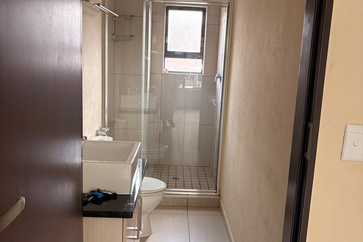 A compact bathroom featuring a glass shower enclosure, vanity cabinet with countertop basin, and neutral floor and wall tiling.