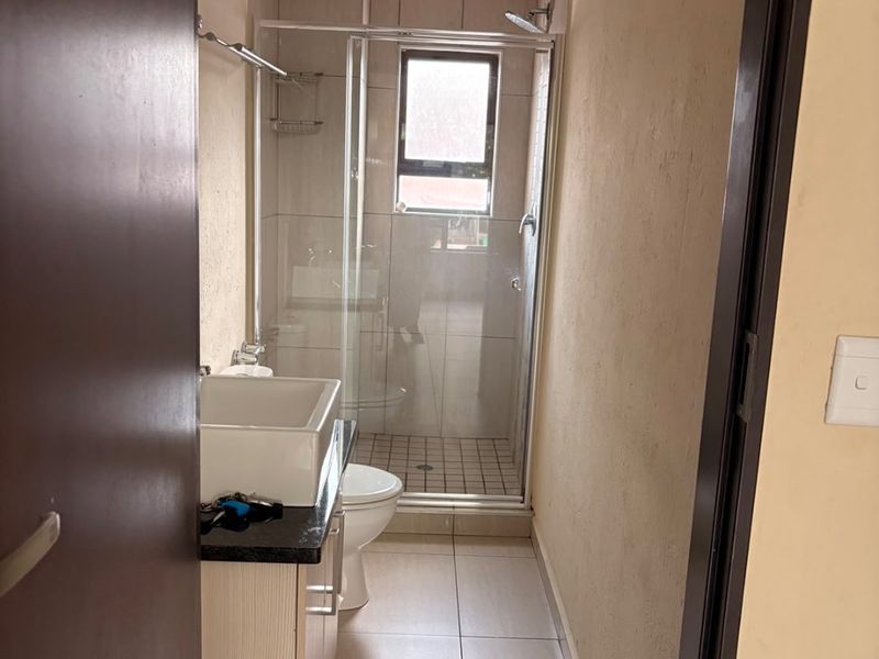 A compact bathroom featuring a glass shower enclosure, vanity cabinet with countertop basin, and neutral floor and wall tiling.