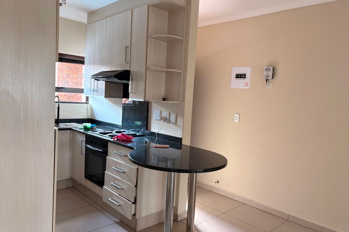 Compact kitchen featuring light wood cabinetry, granite countertops, integrated oven and stove, and a convenient breakfast bar, finished with neutral floor tiles.